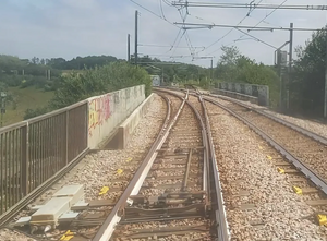 A curved dual track on a bridge, with a single track branching from the left track and crossing over the right track