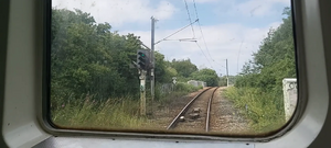 An uphill and slightly curved track with a 3-aspect signal alongside it labelled 764 and showing a green (proceed) aspect, with a radio changeover board behind it, seen through a white window frame
