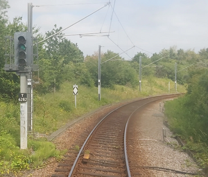 A downhill and curved track, with a 4-aspect signal alongside it labelled T6282 and displaying a green (proceed) aspect, with a radio changeover board behind it